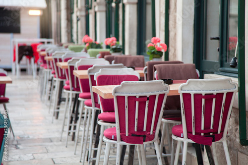 Street cafe in old town outside. Wooden table and red chairs with plaids near windows. Cozy festive atmosphere in Dubrovnik, Croatia. © Marina April