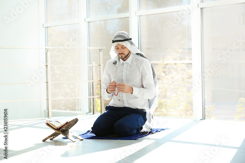 Muslim man with Koran praying on rug indoors