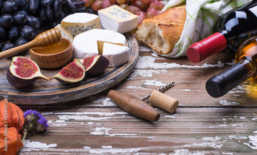 Two bottles with red and white wine with fresh organic natural fruits, delicious cheese on a wooden background with place for text. Flat lay