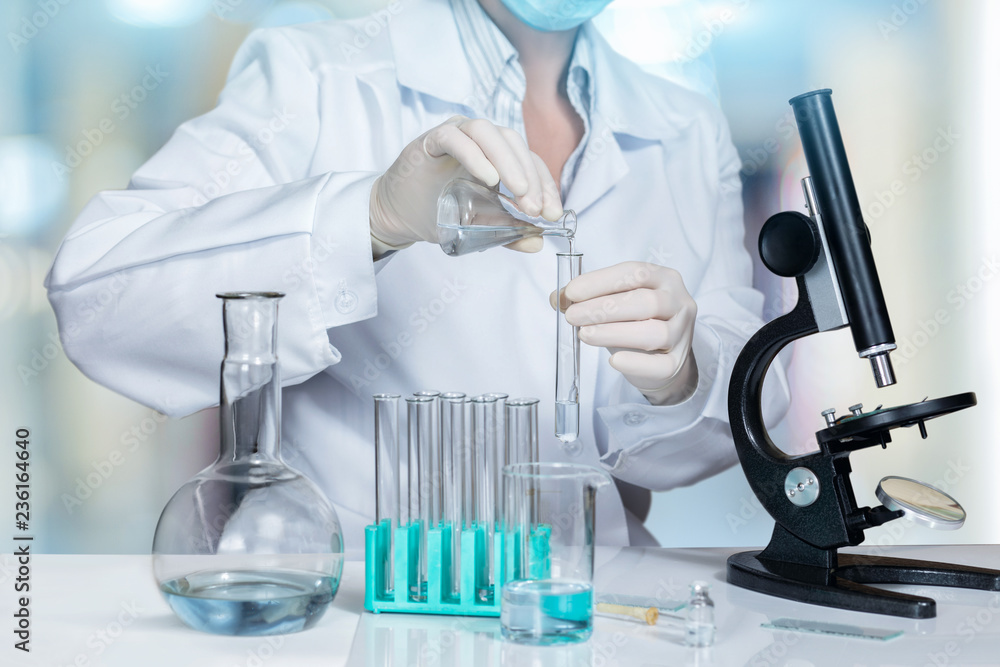 A laboratory assistant is making some experiments with a microscope and substances in test tubes and flasks.