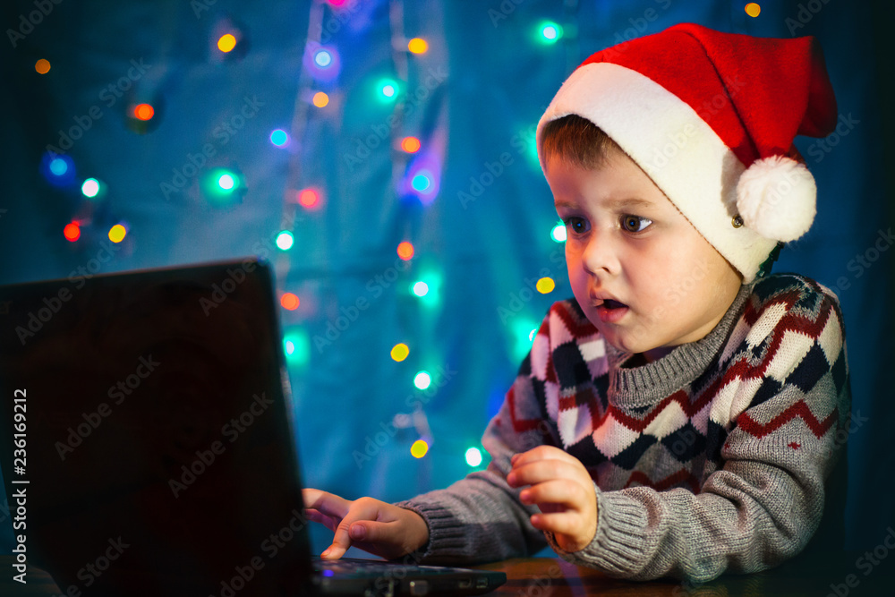 Little child writing letter to Santa Claus on laptop computer. Little boy with santa hat. Little child writing letter to Santa Claus on laptop computer. Little boy with santa hat.