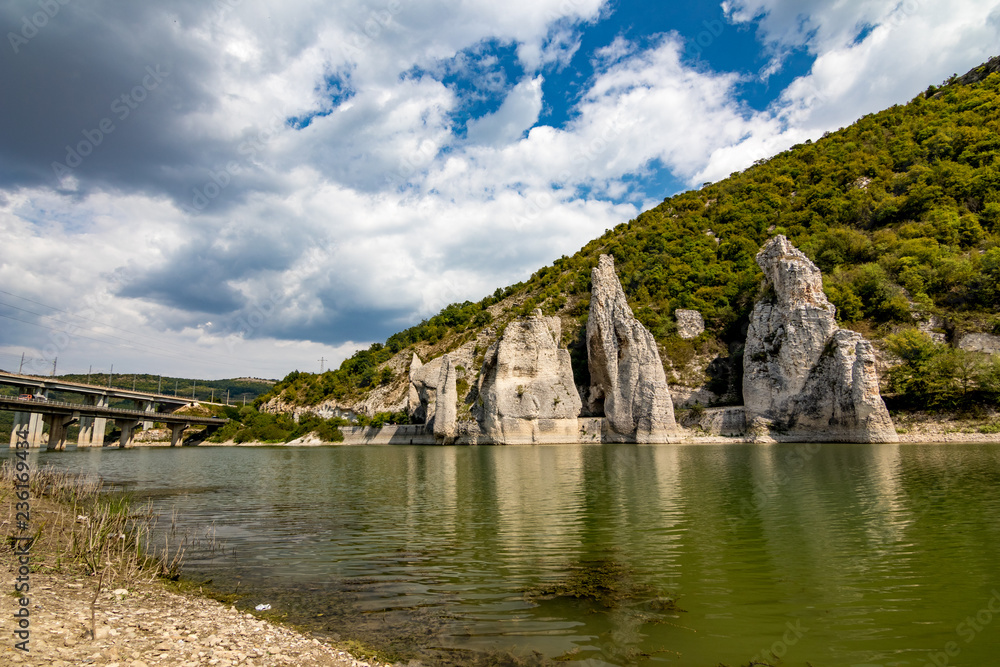 Autumn landscape at the Chudnite Skali natural phenomenon, a.k.a Wonderful Cliffs, Bulgaria, scenery cloudy sky with white clouds, green water with rocks refection and still green mountain hills