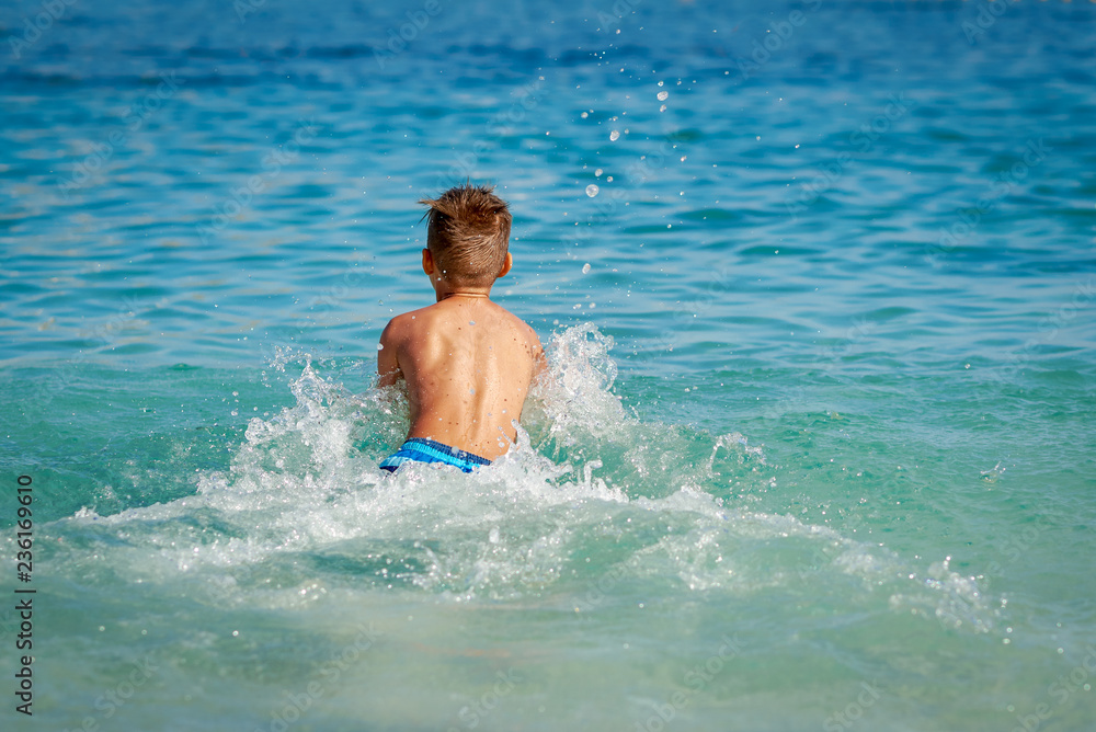 Cute European boy in a striped swimming pants spending his holidays at the sea. He is swimming in the water making a lots of splashes around.