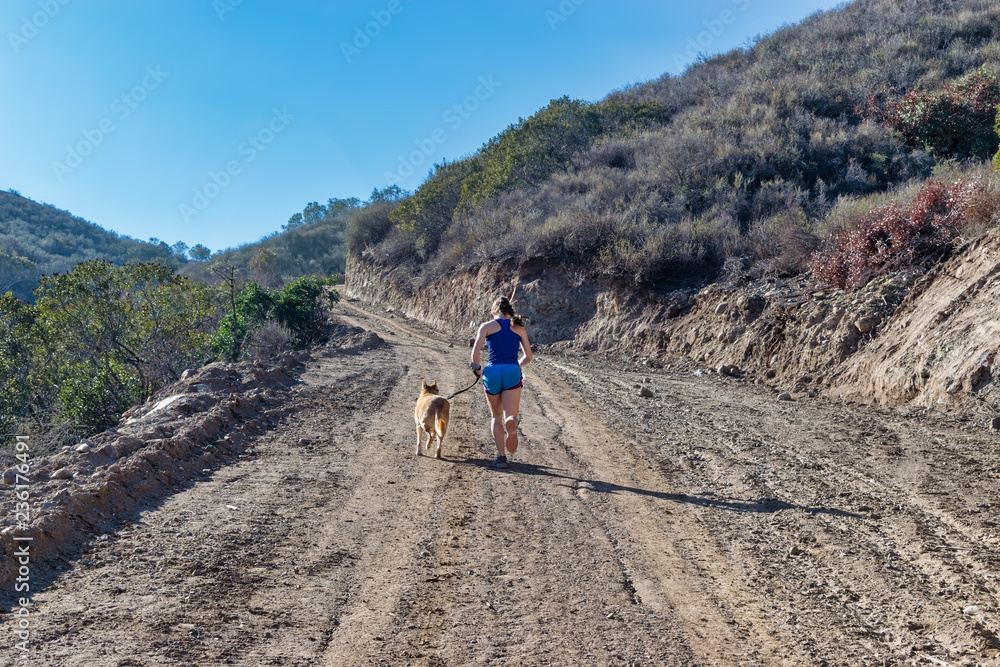 Young woman running up a steep dirt hill with her dog 