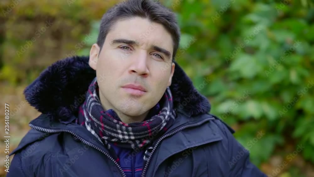 adult pensive man with short dark hair is sitting in park in fall day, looking at camera adult pensive man with short dark hair is sitting in park in fall day, looking at camera
