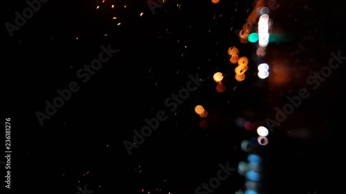 Rain drops on window with road light bokeh, City life in night in rainy season abstract background,water drop on the glass, night storm raining car driving concept.