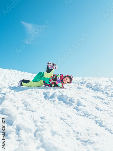 Little girl have fun when slides down from snow hill. She is happy smiling and falling down from her sled