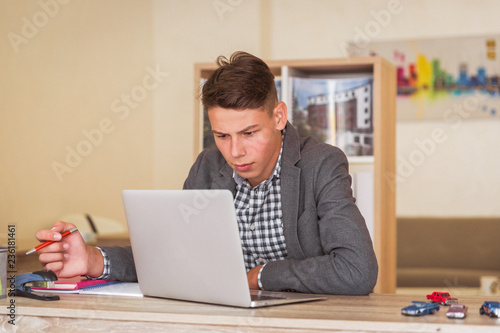 Portrait of the young man who is sitting at the table and working with the laptop indoor