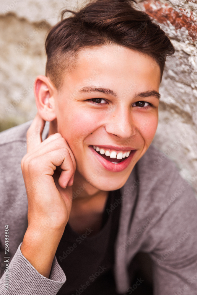 Close-up of the smiling young man who is sitting outdoor near the old house wall Close-up of the smiling young man who is sitting outdoor near the old house wall