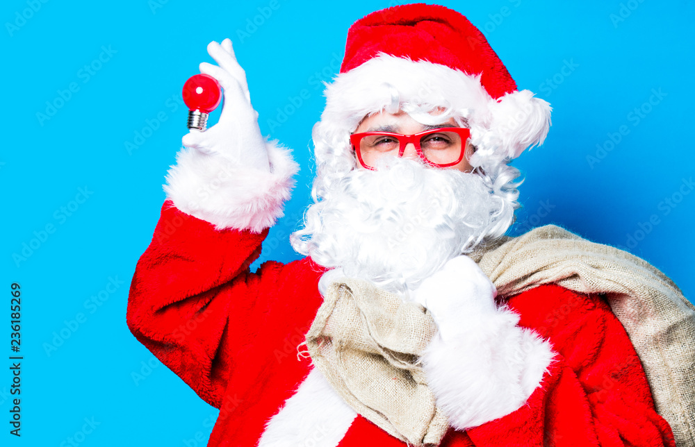 Funny Santa Claus have a fun with light bulb on blue background Funny Santa Claus have a fun with light bulb on blue background