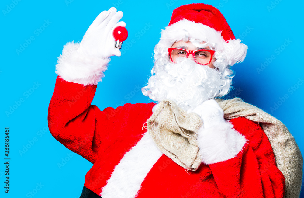 Funny Santa Claus have a fun with light bulb on blue background Funny Santa Claus have a fun with light bulb on blue background