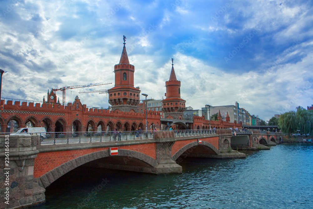 Fototapeta premium Beautiful red brick bridge. Towers with decorations and weathercocks. Cityscape with river and original architecture.