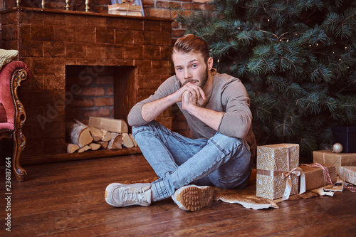 Fotografie A young handsome man looking at a camera while sitting on a floor surrounded by