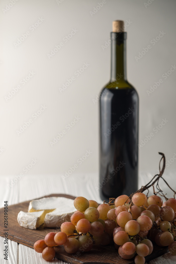 Obraz premium Bottles of wine on a white wooden background with grapes and Camembert cheese