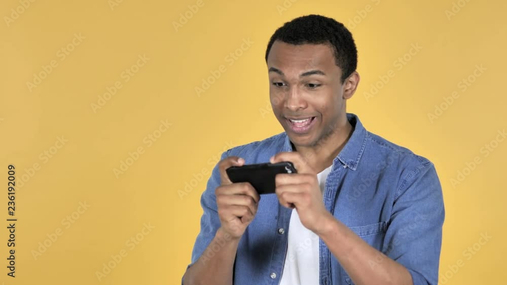 Young African Man Playing Game on Smartphone Isolated on Yellow Background Young African Man Playing Game on Smartphone Isolated on Yellow Background