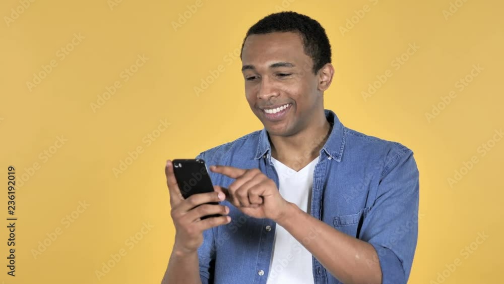 Young African Man Browsing Smartphone Isolated on Yellow Background Young African Man Browsing Smartphone Isolated on Yellow Background