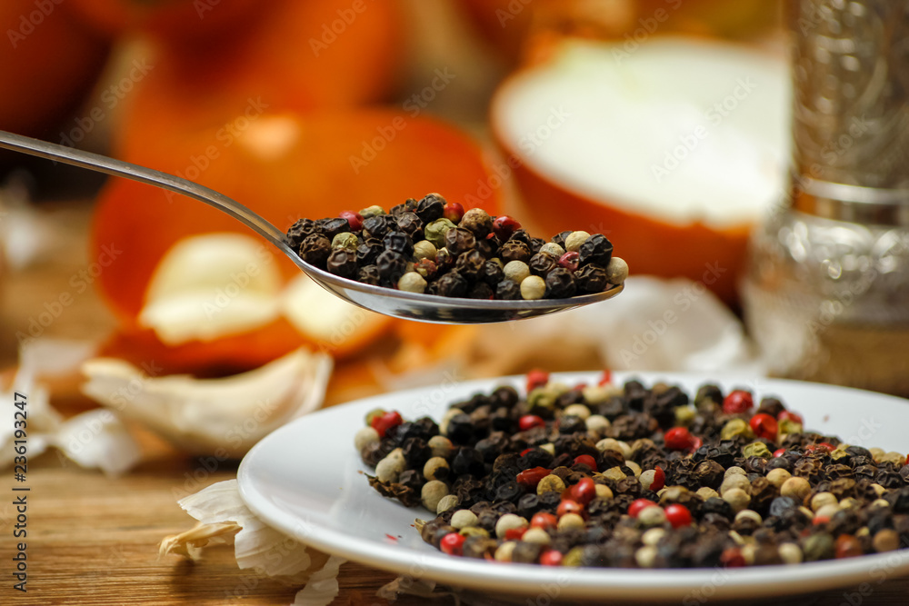 Colored peppers spice mix in spoon and on small ceramic plate. Old wooden table and various of vegetable in the background with red black and white peppercorn. Colored peppers spice mix in spoon and on small ceramic plate. Old wooden table and various of vegetable in the background with red black and white peppercorn.