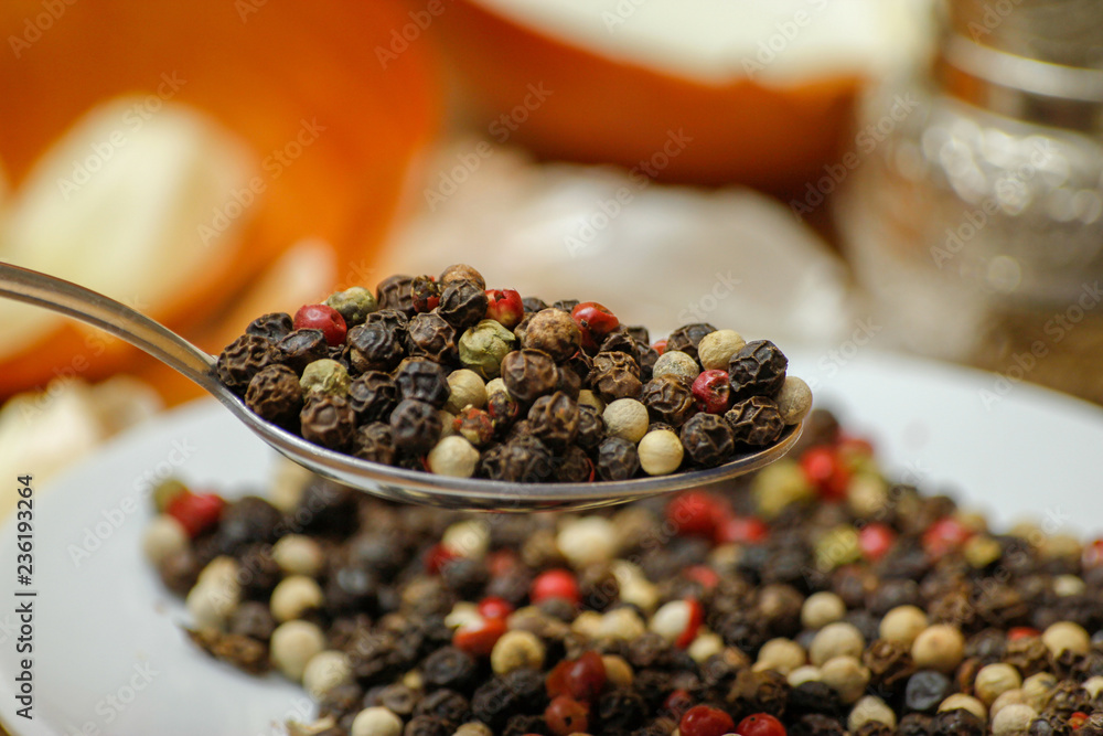 Colored peppers spice mix in spoon and on small ceramic plate. Old wooden table and various of vegetable in the background with red black and white peppercorn. Colored peppers spice mix in spoon and on small ceramic plate. Old wooden table and various of vegetable in the background with red black and white peppercorn.