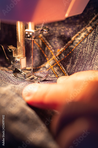Repair jeans on the sewing machine. View of the fabric  needle and thread. Illumination from the built-in incandescent lamp. Jeans are a type of trousers  typically made from denim or dungaree cloth.