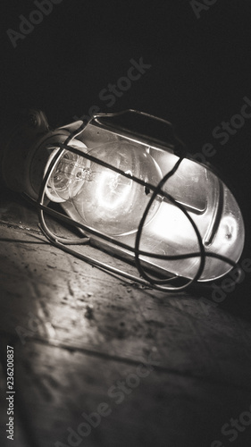 Light bulb in metal case on tiles in car mechanic workshop. Black and white