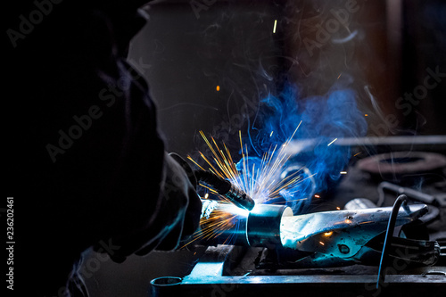 Male worker wearing protective gloves while repairing car exhaust pipe with welding machine