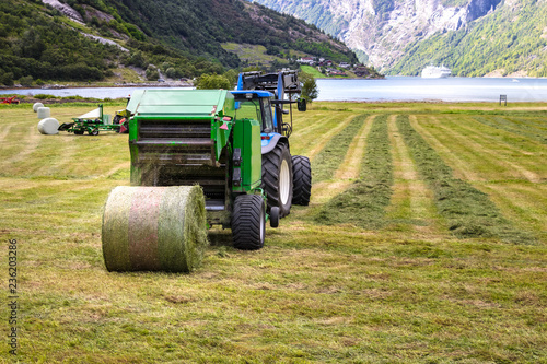 Small tractor with round baler unloading on a field in Geiranger, Norway.