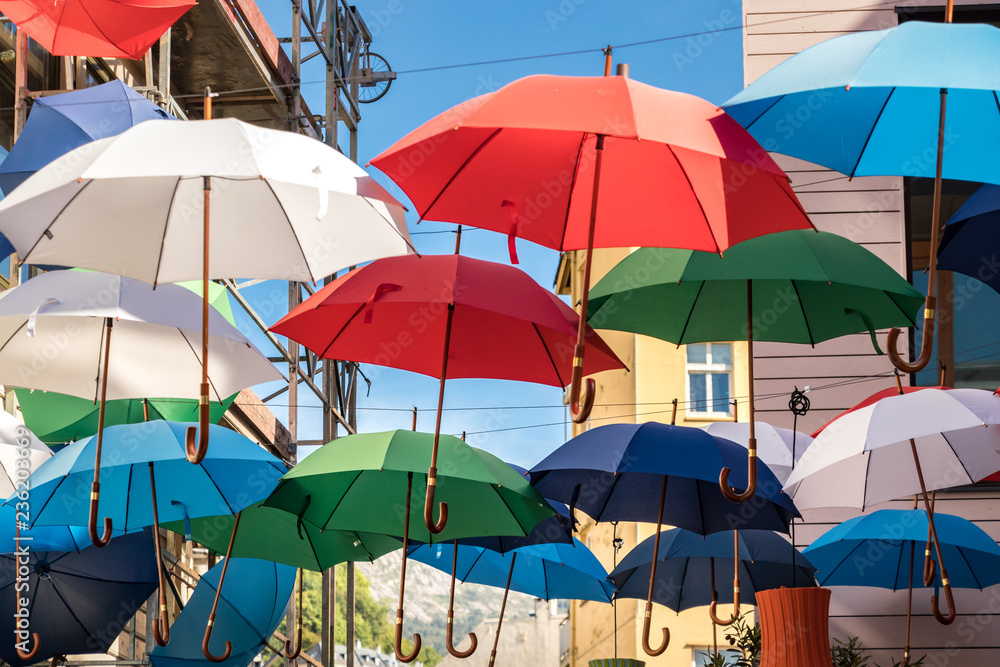 A group of umbrellas hanging on wires multicolored outside on the street.