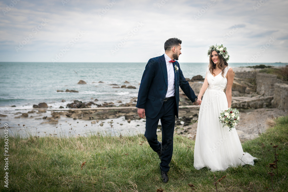 young couple bride groom getting married wedding posed photos at seaside sea beach hairpiece flowers bouquet church