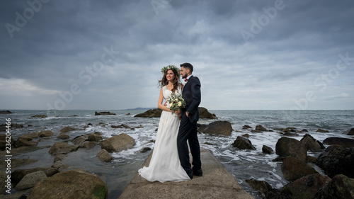 Obraz na płótnie young couple bride groom getting married wedding posed photos at seaside sea beach hairpiece flowers bouquet church w salonie