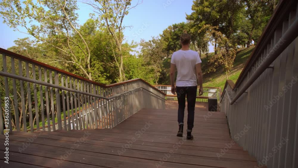 young fair haired man wearing jeans walking in city park. back view trendy guy summer season in town young fair haired man wearing jeans walking in city park. back view trendy guy summer season in town