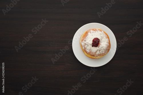 Tradition Jewish holiday sweets, donut sufganioyt with sugar powder and jam on dark wood background top view with copy space. photo