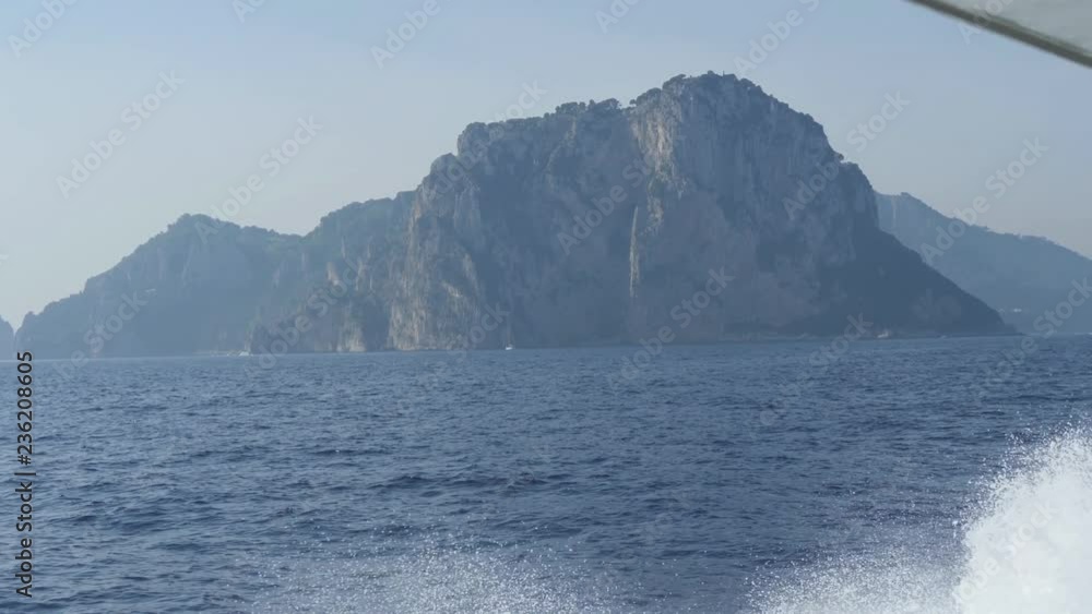 Steep cliff on shores of Capri. Mountain over blue sea. Boat comes up to island. Monte Tiberio, Italy Steep cliff on shores of Capri. Mountain over blue sea. Boat comes up to island. Monte Tiberio, Italy