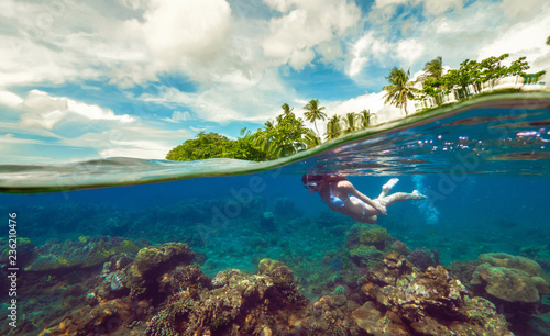 Split underwater photo of a girl snorkeling with mask in tropical ocean enjoying summer vacation on exotic island