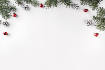 Creative frame made of Christmas fir branches on white background with red decoration, pine cones. Xmas and New Year theme. Flat lay, top view