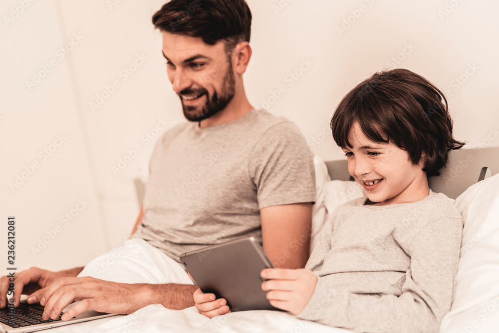 Son with Father Using Laptop in Bed in Morning. Son with Father Using Laptop in Bed in Morning.