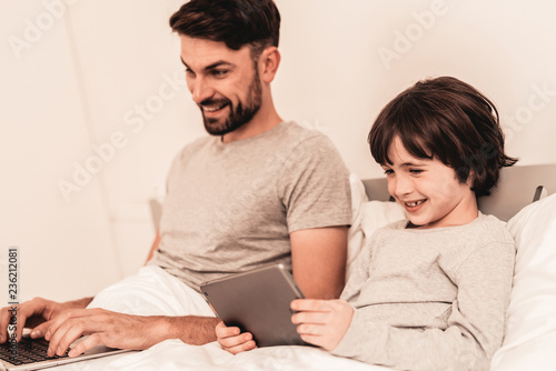 Son with Father Using Laptop in Bed in Morning.