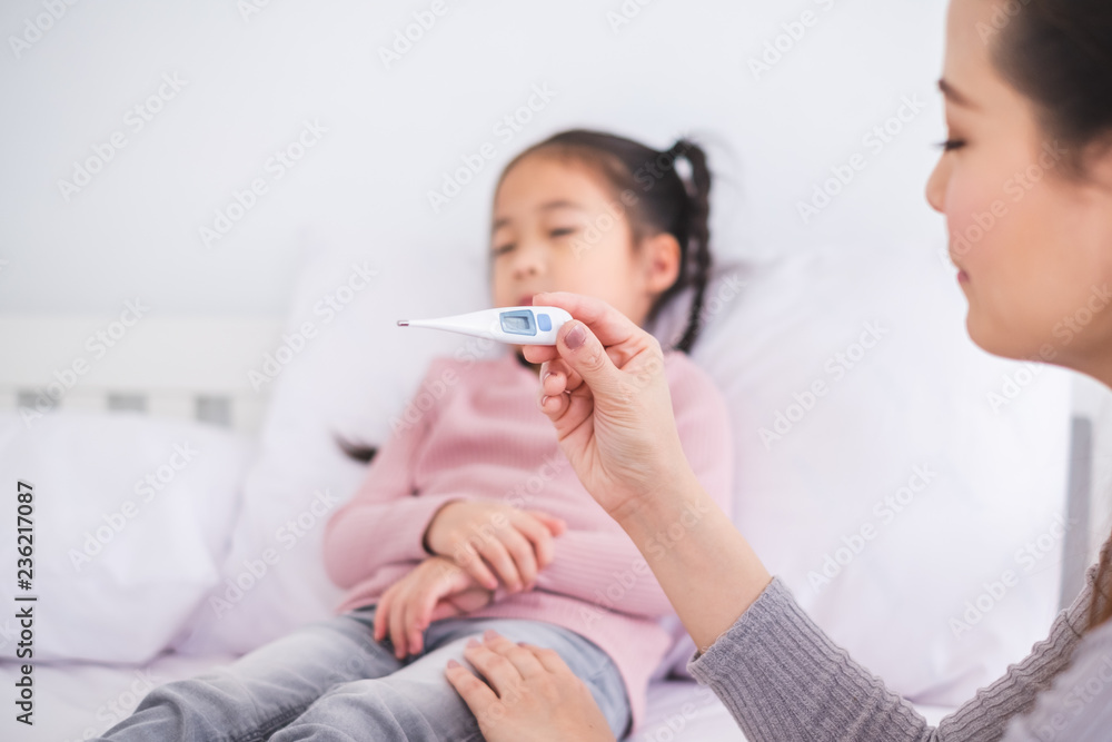 Mother using thermometer with her girl kid daughter for sickness and fever Mother using thermometer with her girl kid daughter for sickness and fever