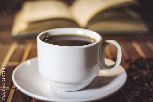 A cup of black coffee on the background of an open book. on a wooden table