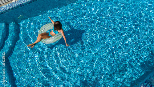 Aerial view of beautiful girl in swimming pool from above, swim on inflatable ring donut and has fun in water on family vacation 