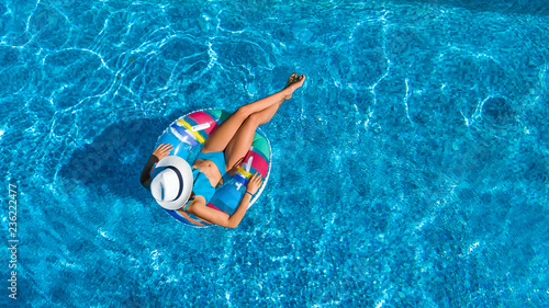 Aerial top view of beautiful girl in swimming pool from above, relax swim on inflatable ring donut and has fun in water on family vacation 