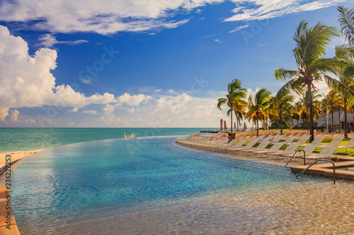 Fototapeta Naklejka Na Ścianę i Meble -  Pool chairs by the turquoise water on a tropical beach and a pool in the Caribbean sea, Freeport, Bahamas