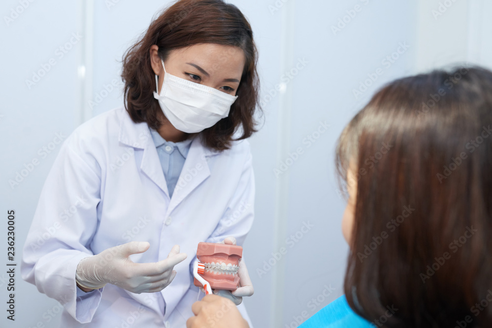 Naklejka premium Doctor explaining young atient how to brush teeth with braces