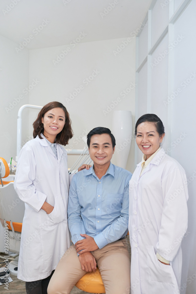 Happy young Asian man and his dentists smiling at camera Happy young Asian man and his dentists smiling at camera