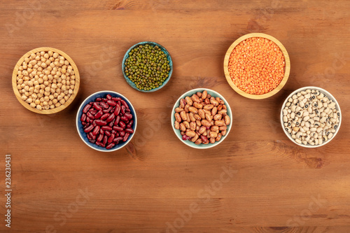 Various pulses, shot from above on a dark rustic wooden background with a place for text. Red kidney and pinto beans, lentils, chickpeas, soybeans, black-eyed peas