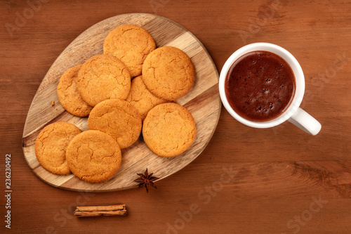 Ginger biscuits with a mug of hot chocolate, a cinnamon stick, and an anise star, shot from the top on a dark rustic wooden background with a place for text