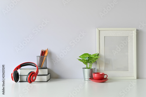 Office stuff with books, coffee, colour pencil, photo frame, headphones and plant on workspace table.