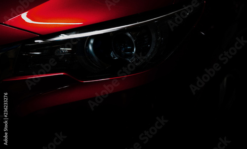 Closeup headlight of shiny red luxury SUV compact car. Elegant electric car technology and business concept. Hybrid auto and automotive concept. Car parked in showroom or motor show. Car dealership. © Artinun