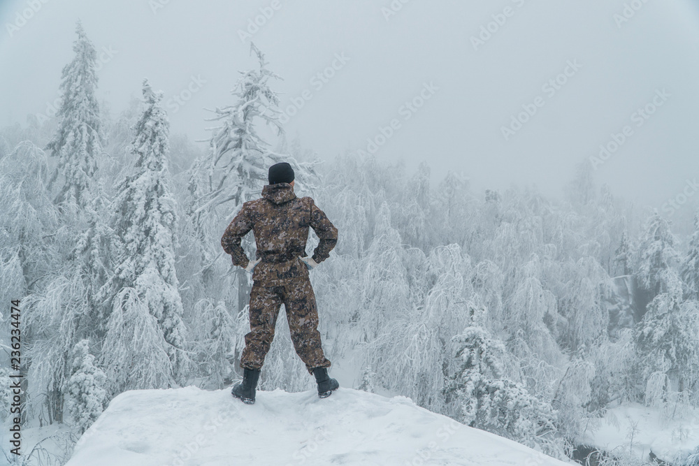 Man hiker standing back on rock in winter mountain landscape, success