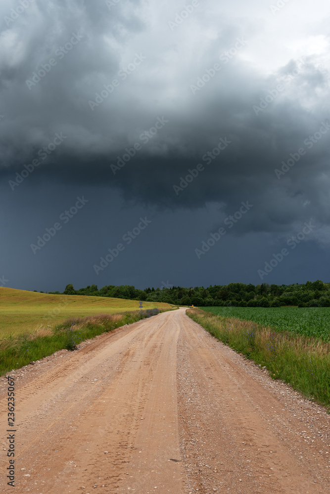 Rural gravel road under stormy summer clouds.