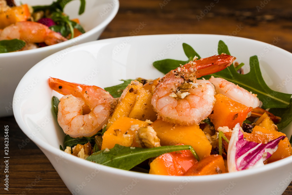 Light fruit salad with fried prawns, persimmon, arugula and walnuts in white bowl on wooden rustic table, close-up Light fruit salad with fried prawns, persimmon, arugula and walnuts in white bowl on wooden rustic table, close-up